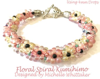 May include: A floral spiral Kumihimo bracelet with pink, yellow, and black beads. The bracelet is designed with a flower pattern and has a silver clasp. The text "Using 4mm Drops" and "Designed by Michelle Whittaker" is visible.