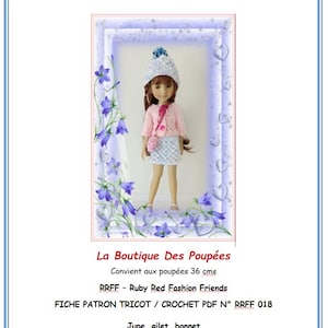 Puede incluir: Una muñeca vestida con un cárdigan de ganchillo rosa claro, un bolso a juego y una falda azul y blanca. La muñeca también lleva un sombrero blanco con un pompón azul. La imagen está enmarcada con un borde azul y detalles florales. El texto en la imagen dice "La Boutique Des Poupées".