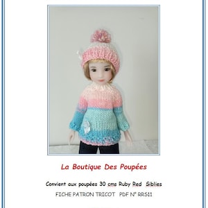 Peut inclure: Une poupée vêtue d'un pull et d'un bonnet tricotés à la main. Le pull présente des rayures horizontales roses, bleues et blanches. Le bonnet est rose et blanc avec un pompon. Le texte "La Boutique Des Poupées" est visible.