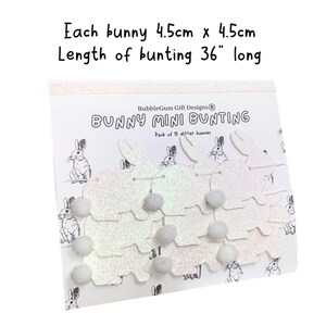 K&ouml;nnte beinhalten: Eine wei&szlig;e Glitzer-Hasen-Mini-Girlande mit 12 Hasen und wei&szlig;en Pompons. Jeder Hase ist 4,5 cm x 4,5 cm gro&szlig; und die Girlande ist 91,44 cm lang. Die Verpackung tr&auml;gt den Schriftzug "BubbleGum Gift Designs&reg; Bunny Mini Bunting Pack of 12 glitter bunnies".