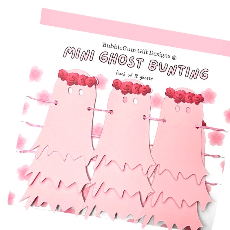 Pode incluir: Guirlanda de fantasmas de papel rosa com uma coroa de flores. A guirlanda diz "Mini Ghost Bunting" e "BubbleGum Gift Designs" com um s&iacute;mbolo de direitos autorais. A guirlanda &eacute; um pacote de 12 fantasmas.