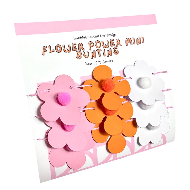 K&ouml;nnte beinhalten: Eine Packung mit 12 bl&uuml;tenf&ouml;rmigen Papierdekorationen mit Pompons in Rosa, Orange und Wei&szlig;. Die Dekorationen sind mit rosa Garn aneinandergereiht und mit "Flower Power Mini Bunting" beschriftet.