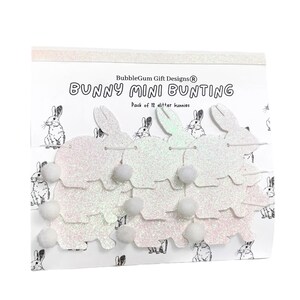K&ouml;nnte beinhalten: Eine Packung mit wei&szlig;en Glitzer-Hasen-Mini-Girlanden. Die Girlande besteht aus wei&szlig;em Glitzerpapier und hat zwischen jedem Hasen einen wei&szlig;en Bommel. Die Verpackung lautet "BubbleGum Gift Designs&reg; Bunny Mini Bunting Pack of 12 glitter bunnies".