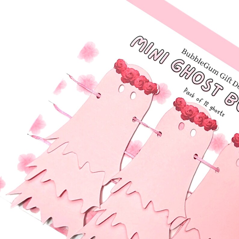 Pode incluir: Guirlanda de fantasmas de papel rosa com uma coroa de rosas, parte de um conjunto de 12 mini decora&ccedil;&otilde;es de fantasmas. O texto na embalagem diz "BubbleGum Gift Decor Mini Ghost Banner Pack of 12 ghosts".