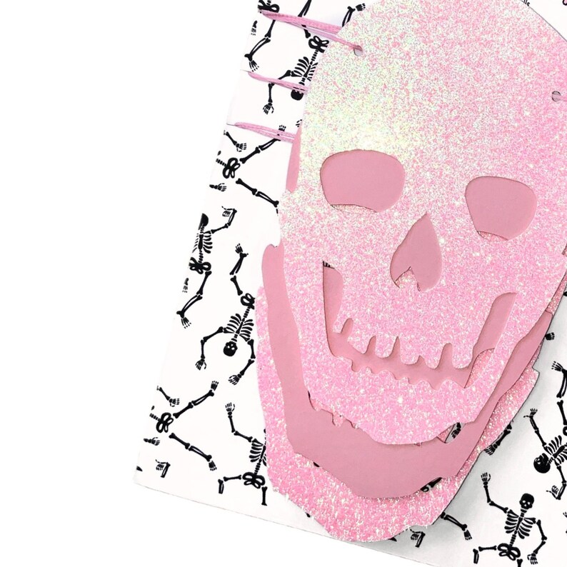 May include: Pink glitter skull with a white background featuring black skeleton silhouettes.