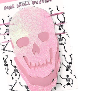 May include: Pink glitter skull bunting with a white background featuring a repeating pattern of black skeletons. The text "PINK SKULL BUNTING" is at the top of the image.