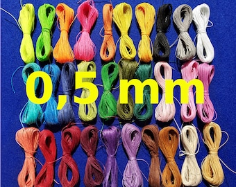Peut inclure: Une collection de 30 bobines de fil à broder coloré, chacune mesurant 0,5 mm d'épaisseur. Le fil est disposé en rangées sur une surface bleue.