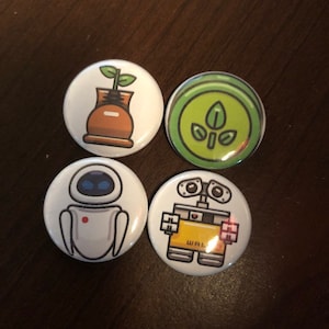 May include: Four round buttons with different images from the Disney Pixar movie Wall-E. The first button has a green plant growing out of a brown pot. The second button has a green plant with three leaves. The third button has a white robot with blue eyes and a red dot on its chest. The fourth button has a yellow robot with the word "WALL-E" printed on its chest.