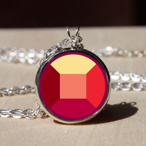 May include: A silver chain necklace with a round pendant featuring a red, orange, and yellow geometric design. The pendant is reminiscent of a gemstone.
