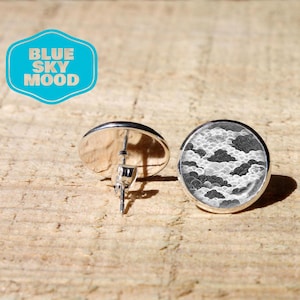Op de afbeelding: Een paar ronde oorknopjes met een zwart-wit grafisch patroon van gestileerde wolken en golven. De oorbellen hebben een zilverkleurige metalen zetting met een stift. De tekst BLUE SKY MOOD is zichtbaar in een blauwe grafische overlay.