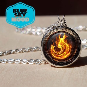 May include: A silver-toned pendant necklace featuring a round pendant with a fiery flame design in shades of orange and yellow against a dark background. The necklace includes a chain and the text "BLUE SKY MOOD" in a blue and white design.