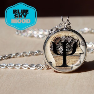 May include: A silver pendant necklace with a round charm displaying a psychology-themed design. The charm features a wooden backdrop, gears, and a black Psi symbol. The text "BLUE SKY MOOD" is in a blue and white logo.