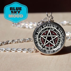 Może przedstawiać: Srebrny naszyjnik z okrągłą zawieszką. Zawieszka ma czarne tło z białym wzorem pentagramu, czerwonym wewnętrznym okręgiem i białymi symbolami. Naszyjnik ma łańcuszek i tekst "BLUE SKY MOOD" w niebieskim pudełku.