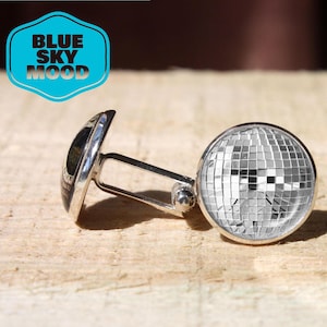 May include: Silver cufflinks with a disco ball design and the text "BLUE SKY MOOD". The cufflinks have a shiny, reflective surface and a classic T-bar closure. The disco ball design is made up of many small, square mirrored tiles.