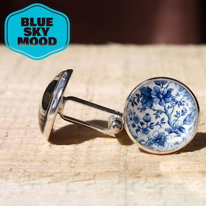 Könnte beinhalten: Silberne Manschettenknöpfe mit rundem, blau-weißem Blumendesign. Ein Manschettenknopf hat ein schwarz-weißes Design. Die Manschettenknöpfe sind durch einen silbernen Steg verbunden. Der Text "BLUE SKY MOOD" ist enthalten.
