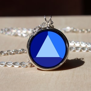 Könnte beinhalten: Eine silberne Kettenkette mit einem runden Anhänger mit einem blauen, weißen und dunkelblauen Dreiecksdesign.