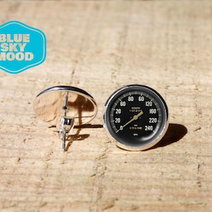 Op de afbeelding: Zilverkleurige oorstekers met een zwart snelheidsmeterontwerp. De snelheidsmeter heeft witte markeringen en cijfers op een zwarte achtergrond, met een zilveren rand. De tekst "BLUE SKY MOOD" staat in een blauwe bubbel.
