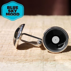 May include: Silver cufflinks featuring a black vinyl record design. The cufflinks have a circular face with a detailed record graphic and a silver backing. The image also includes a blue and white logo that says "BLUE SKY MOOD".