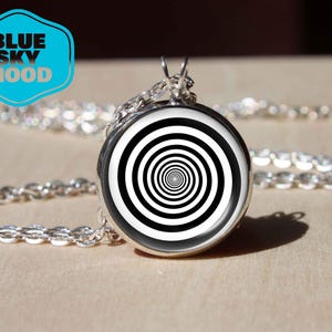 Può includere: Una collana con catena d'argento con un ciondolo rotondo con un motivo a spirale bianco e nero.