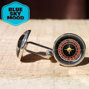 May include: Silver cufflinks with a roulette wheel design. The cufflinks have a black background with red and white numbers, and a gold-colored center. The text "BLUE SKY MOOD" is in a blue hexagon in the upper left.