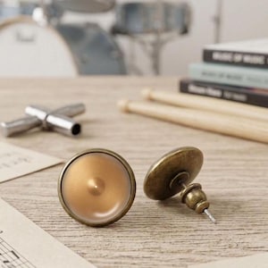 Può includere: Un paio di orecchini a lobo rotondi con un centro color oro metallizzato liscio e una sottile trama circolare radiante. Gli orecchini presentano una finitura in bronzo scuro in stile antico sul bordo esterno e sul meccanismo di chiusura.