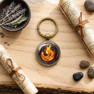 May include: A circular keyring featuring a bronze-toned metal frame and a glass cabochon insert. The insert displays a vibrant, detailed graphic of swirling orange and yellow flames set against a dark, contrasting background.