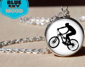 May include: Silver-toned pendant necklace featuring a circular pendant with a black silhouette of a mountain biker on a white background. The necklace has a chain and the text "BLUE SKY MOOD" in a blue and white design.