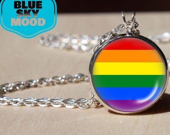 Puede incluir: Un collar plateado con un colgante redondo con un diseño de arcoíris. El colgante está engastado en un marco plateado y cuelga de una delicada cadena. La imagen también incluye un logotipo azul y blanco que dice "BLUE SKY MOOD".