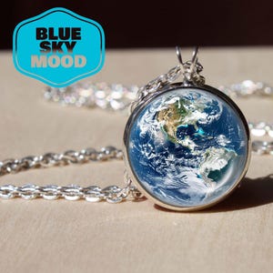 May include: A silver-toned pendant necklace featuring a round glass globe with a detailed image of Earth. The globe is suspended from a delicate chain. The text "BLUE SKY MOOD" is in a blue and white graphic in the upper left corner.