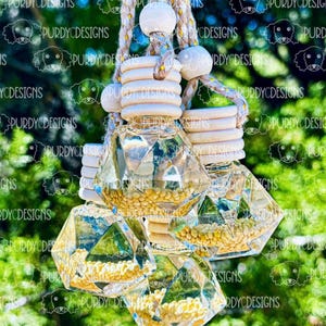 以下が含まれることがあります： 黄色いビーズが入った透明なダイヤモンド型の車の芳香剤が4つ。芳香剤は、木製のビーズが付いたベージュのロープにぶら下がっています。