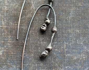 May include: A pair of silver earrings with a delicate, curved design. Each earring features multiple small, textured spheres.