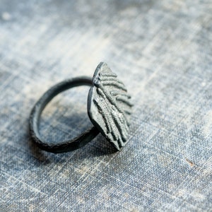May include: A silver ring with a textured, abstract design. The ring is made of metal and has a wide band.