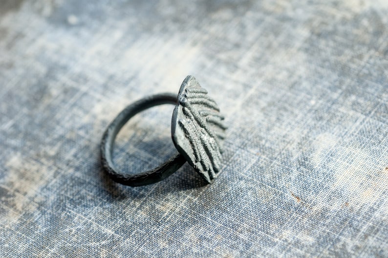 May include: A silver ring with a textured, abstract design. The ring is made of metal and has a wide band.