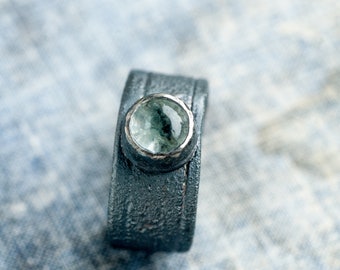 May include: A silver ring with a textured band and a round, light green gemstone.