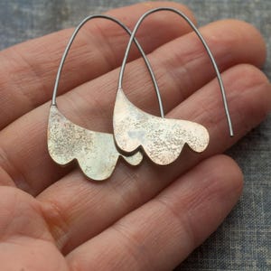 May include: A pair of silver earrings with a textured, organic shape. The earrings are made of metal and have a delicate, flowing design.