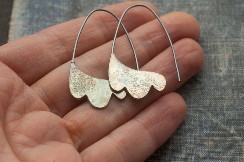 May include: A pair of silver earrings with a textured, organic shape. The earrings are made of metal and have a delicate, flowing design.