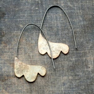 May include: A pair of earrings with a unique, organic shape. The earrings are made of a textured metal with a gold finish and hang from silver-toned wires.
