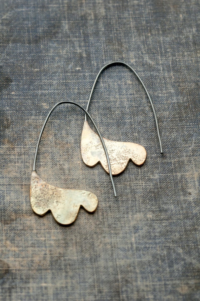 May include: A pair of earrings with a unique, organic shape. The earrings are made of a textured metal with a gold finish and hang from silver-toned wires.