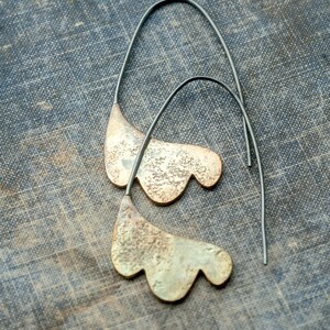May include: A pair of silver earrings with a unique, organic shape resembling a leaf. The earrings are made of metal and have a textured surface.