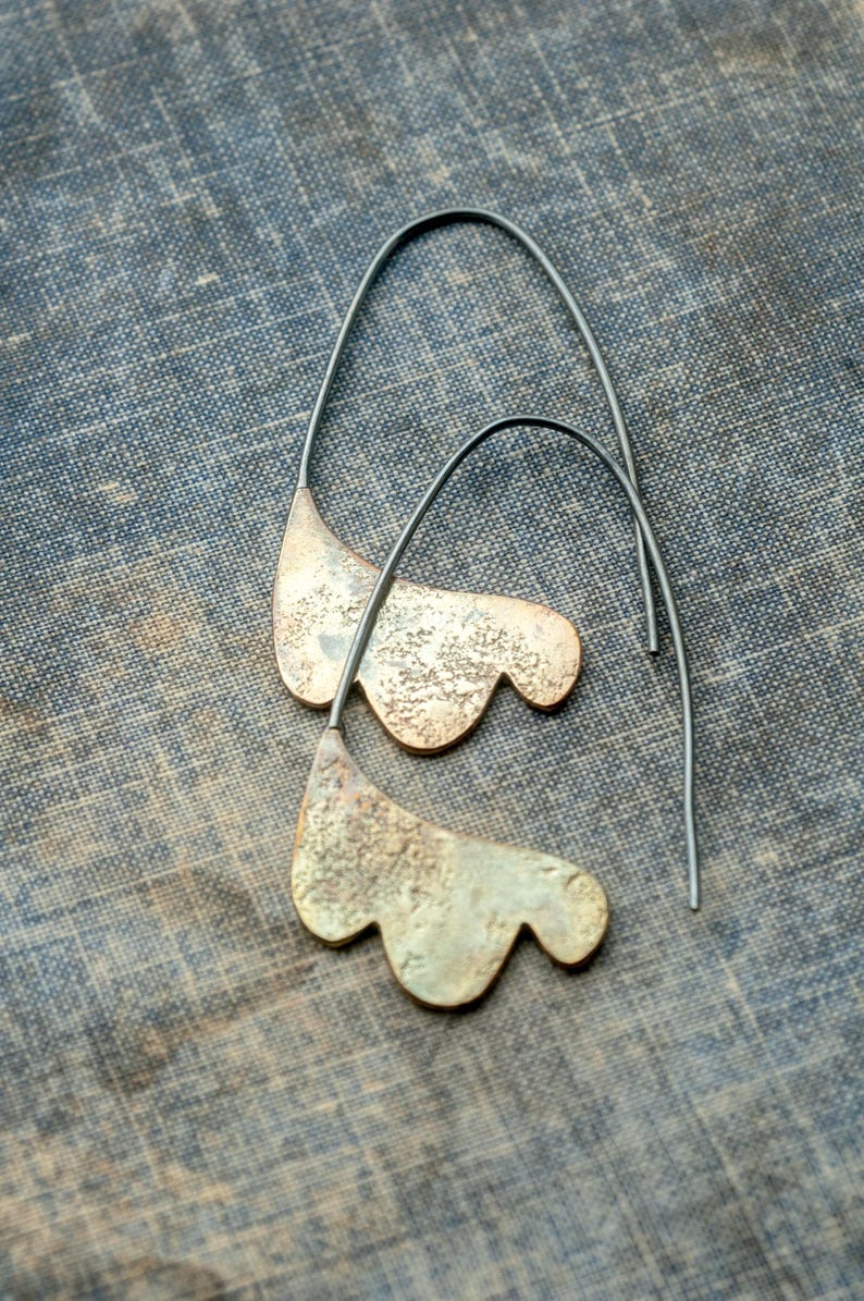 May include: A pair of silver earrings with a unique, organic shape resembling a leaf. The earrings are made of metal and have a textured surface.