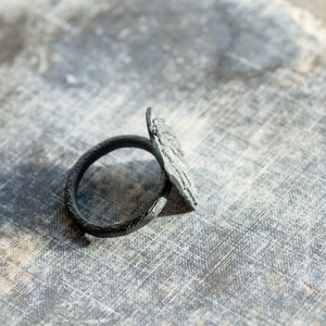 May include: A black metal napkin ring with a decorative design. The ring is lying on a textured surface.