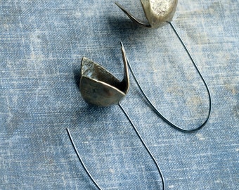 Puede incluir: Un par de pendientes de plata con un diseño único y abstracto. Los pendientes están hechos de metal y tienen un acabado texturizado. Los pendientes cuelgan de un bucle de alambre.