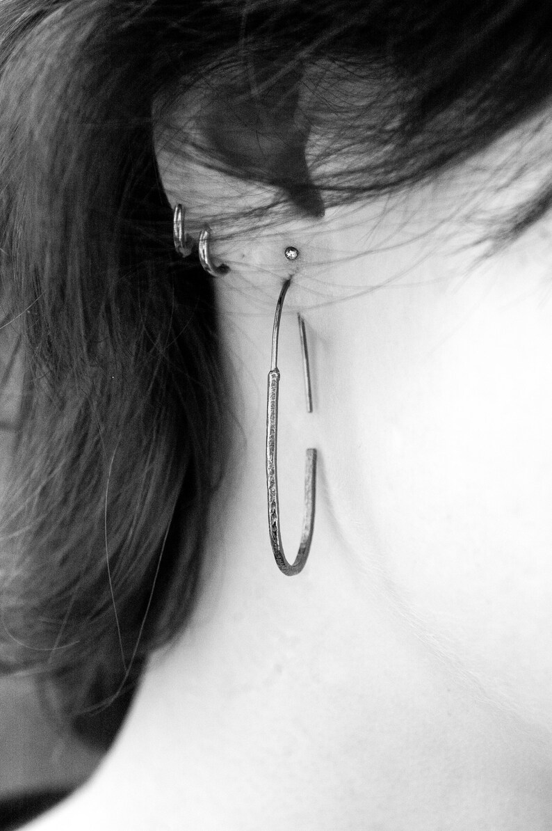 Pu&ograve; includere: Primo piano di un orecchio con pi&ugrave; piercing. La persona indossa un grande orecchino a cerchio d'argento nell'orecchio superiore.