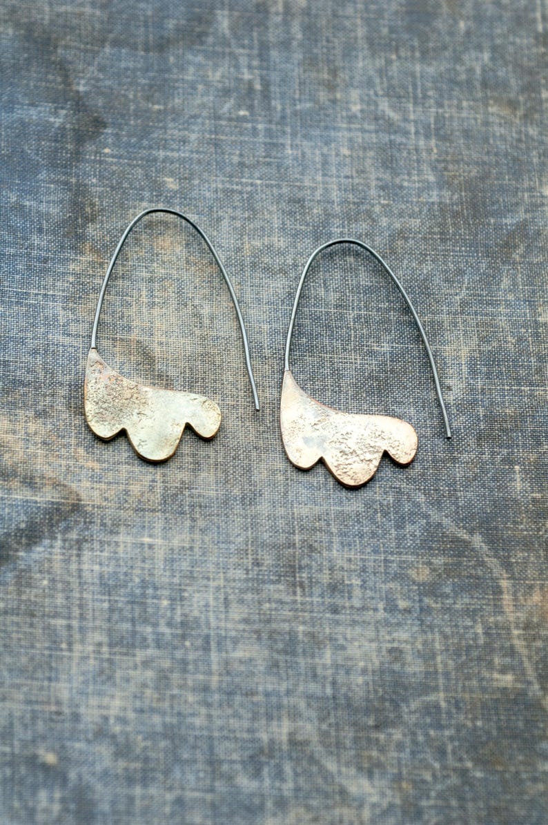 May include: A pair of silver earrings with a textured, organic shape. The earrings are suspended from thin black wires.