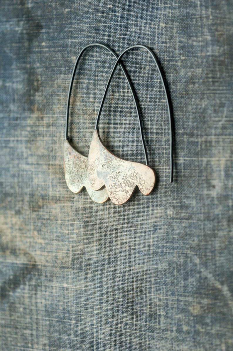 May include: A pair of silver earrings with a unique, organic shape and a textured finish. The earrings are suspended from black wire hoops.