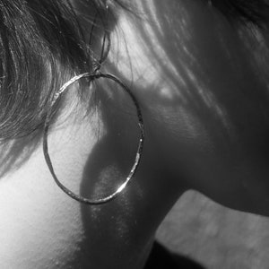 Puede incluir: Primer plano de la oreja de una persona con un aro de plata. El aro es grande y tiene una textura martillada.