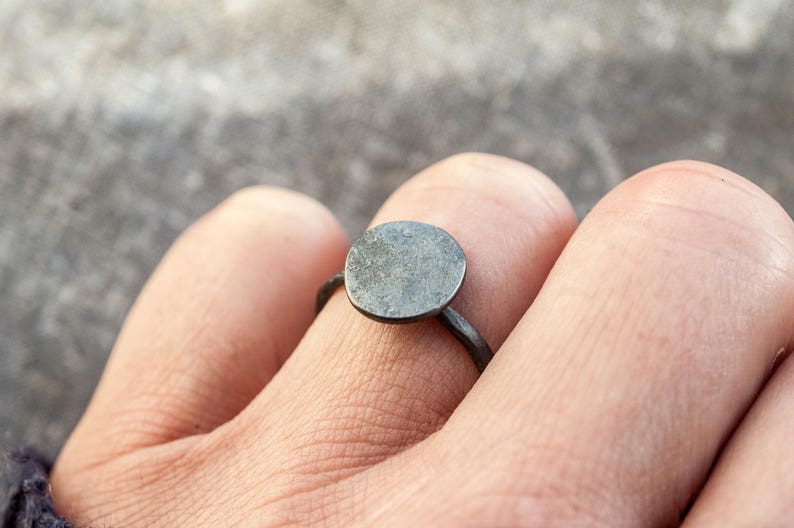 May include: A simple silver ring with a round, flat top. The ring is worn on a finger.