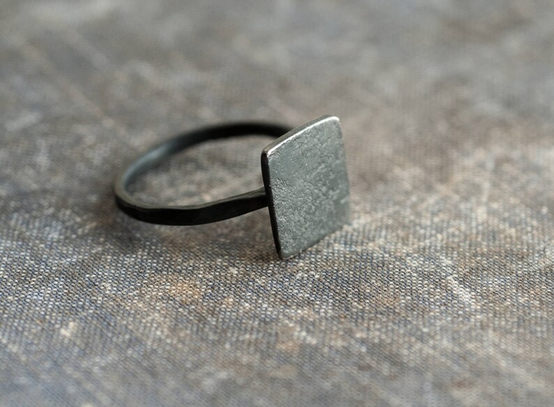 Puede incluir: Un anillo cuadrado negro con una superficie texturizada.