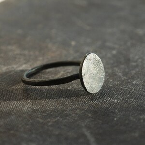 May include: A silver ring with a textured oval-shaped top. The ring band is black.
