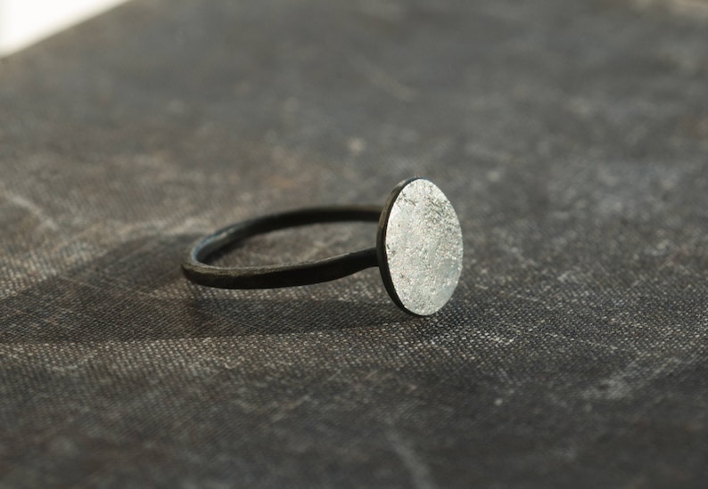 May include: A silver ring with a textured oval-shaped top. The ring band is black.
